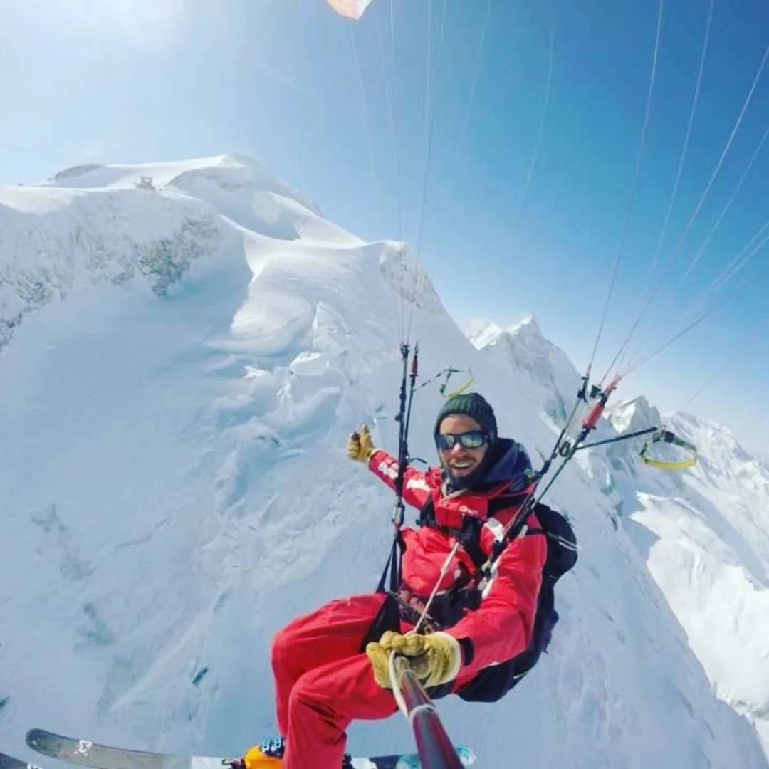 Moniteur de parapente skis aux pieds en vol au-dessus des crêtes enneigées